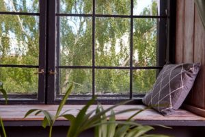 A picture of large windows with handles, trees in the background, and a pillow against a wood wall.